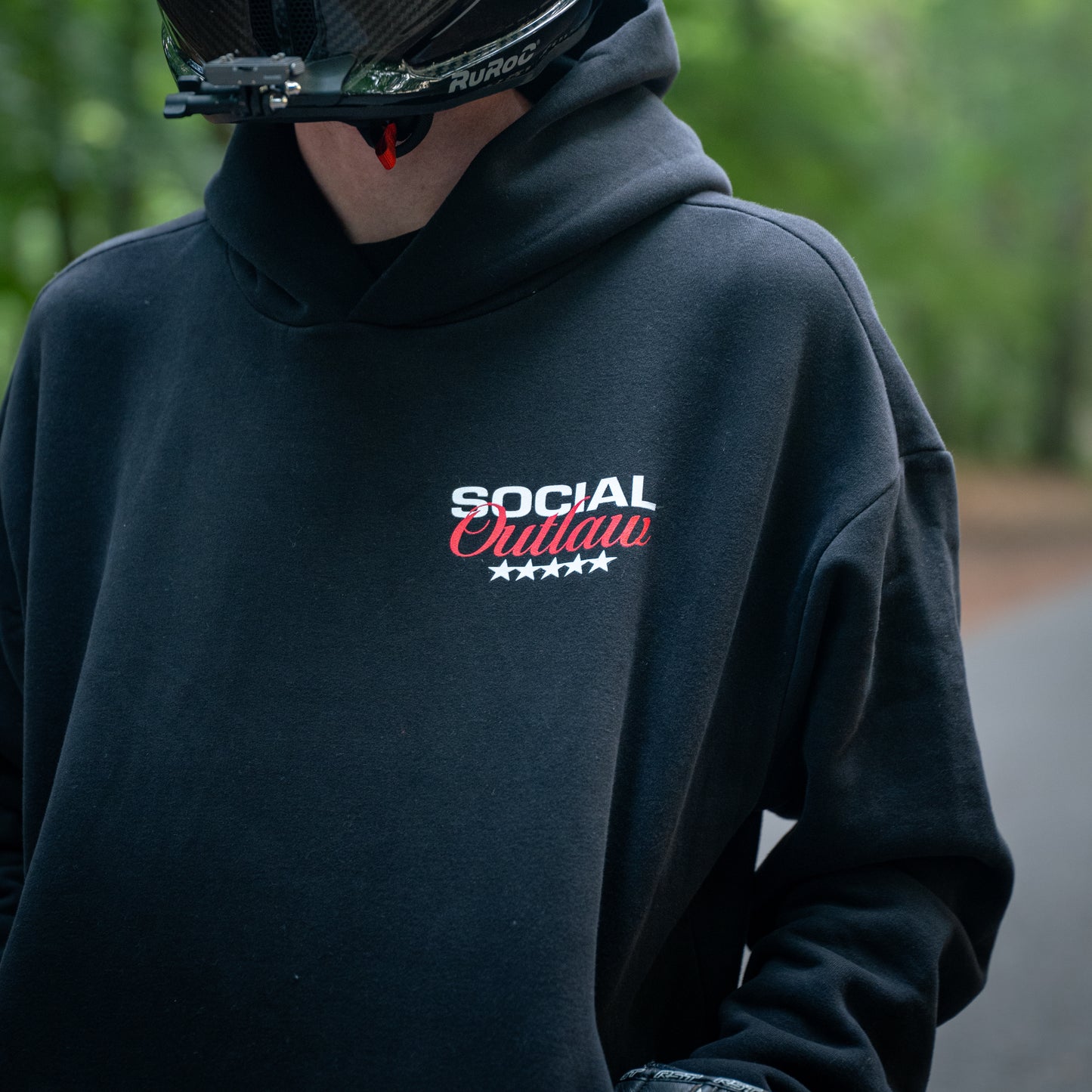 Person wearing a black hoodie with 'Social Outlaw' text, standing outdoors.