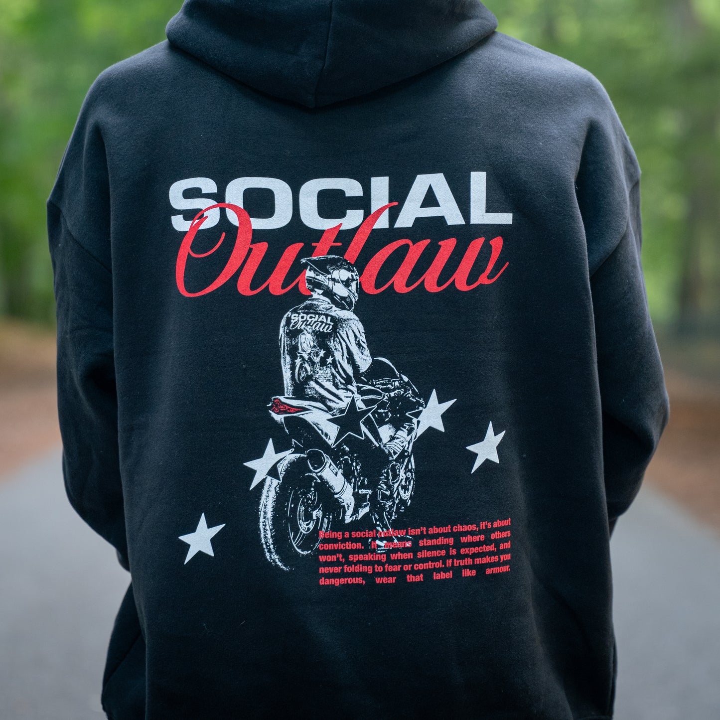 Black hoodie with 'Social Outlaw' graphic and text on the back, worn by a person outdoors.
